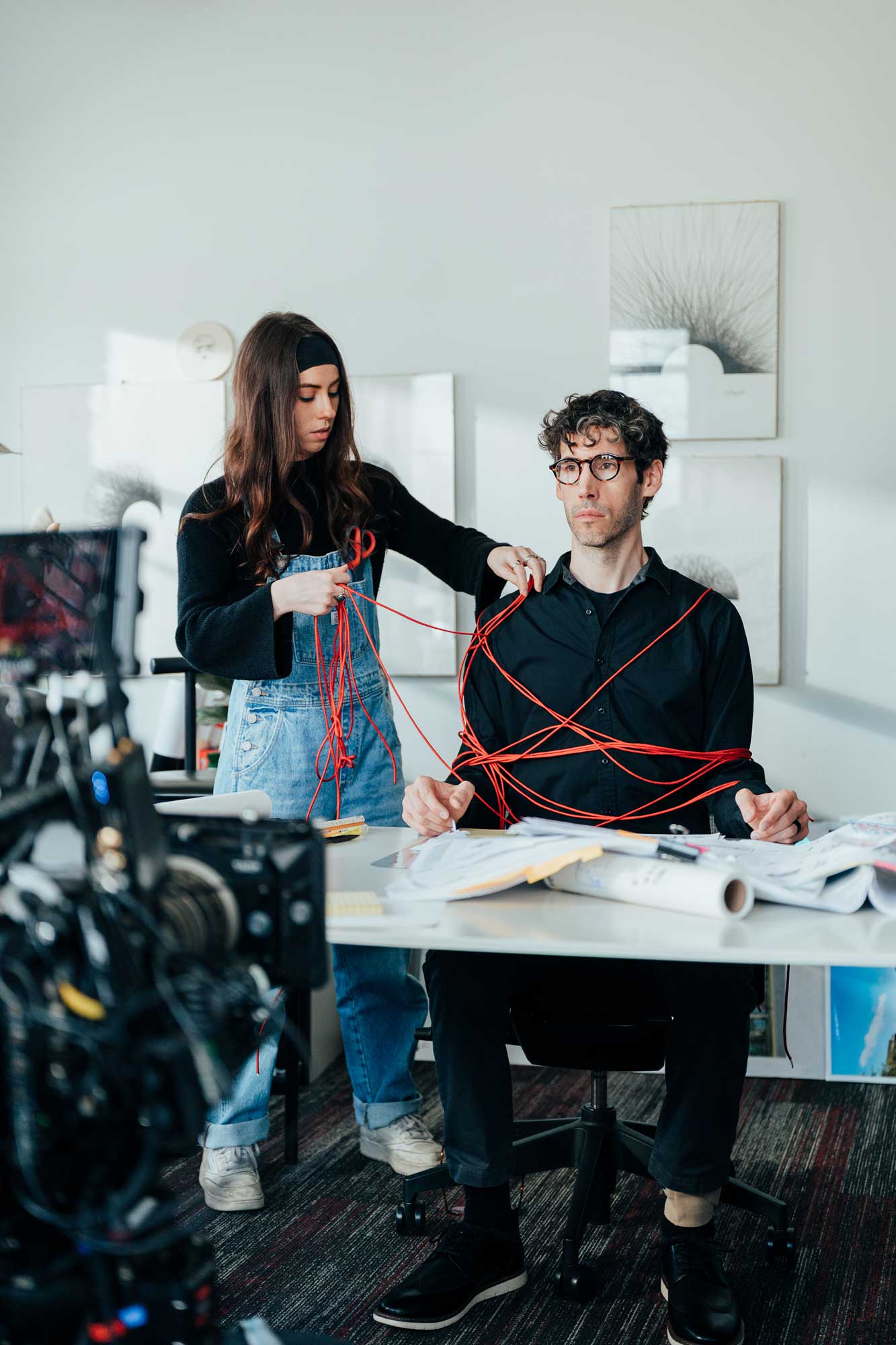 Behind the scenes of the Redline Mayhem sketch — an architect literally tangled in red string while a producer untangles the chaos