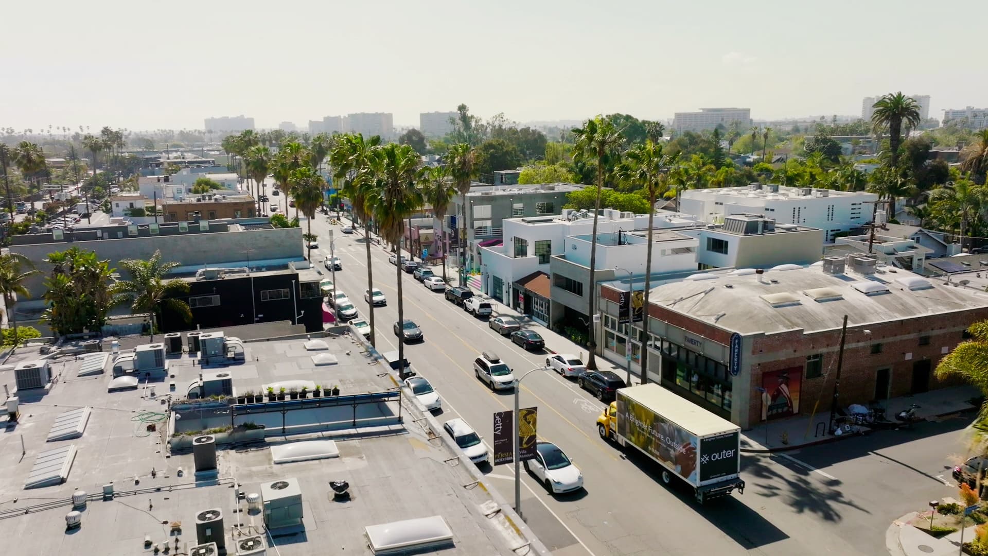 Drone aerial of a Los Angeles commercial street with palm trees and rooftop businesses